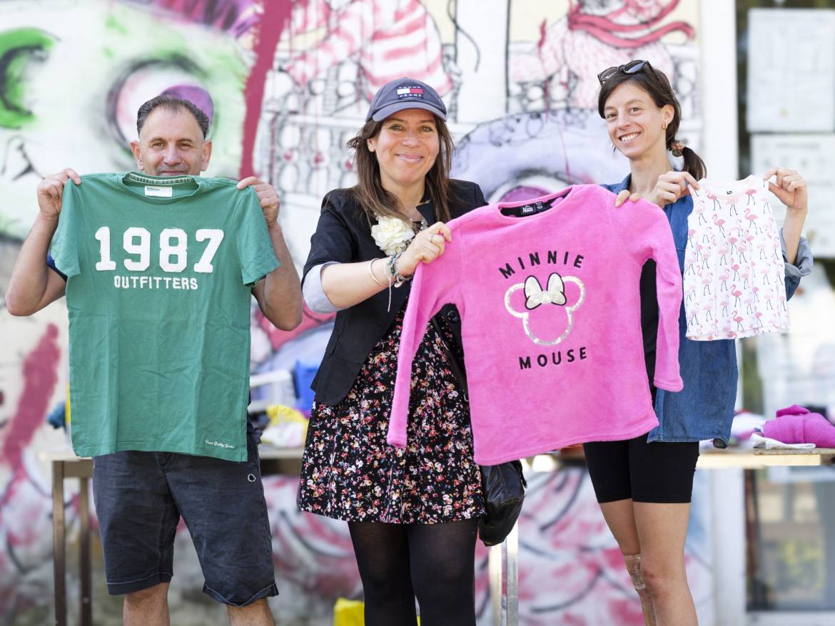 Trois personnes tiennent des vêtements pour femmes, hommes et enfants dans les mains.